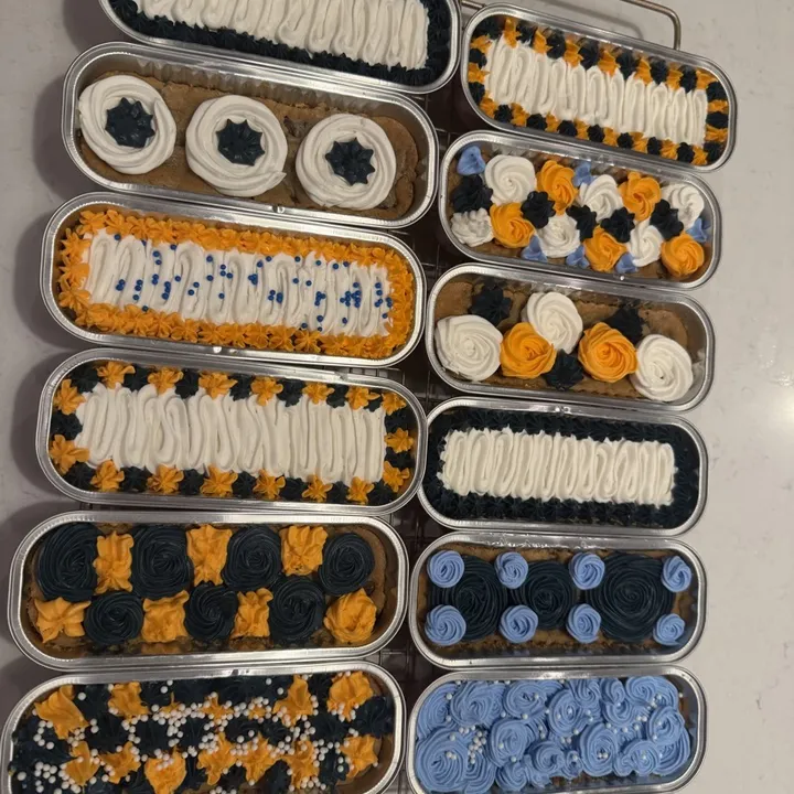 A dozen mini cookie cakes in tins, piped in navy, orange, white and light blue