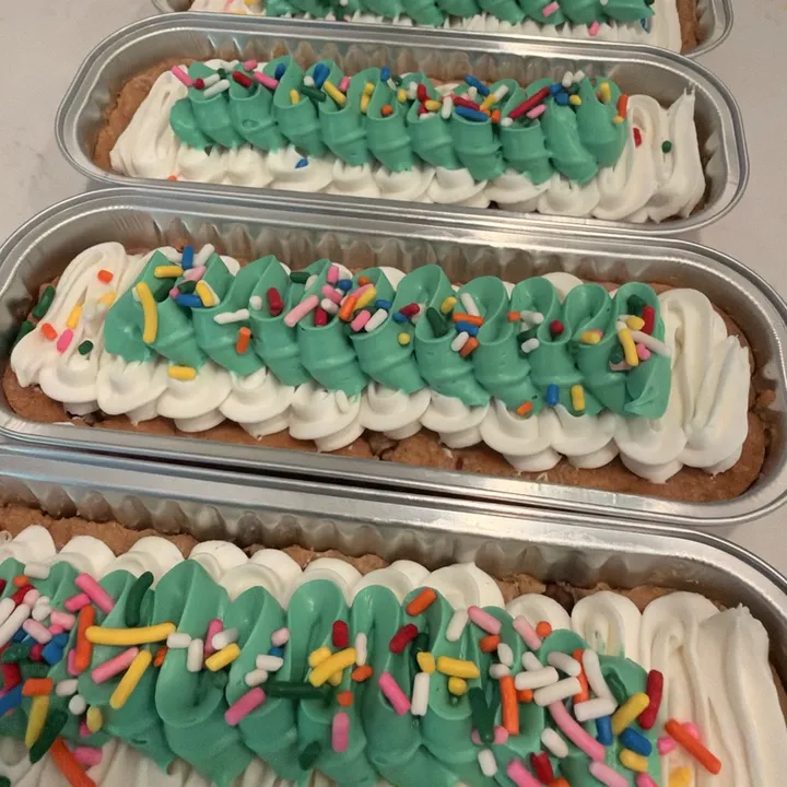 Cookie cakes with a green ribbon swirl over white ruffles, topped with rainbow sprinkles